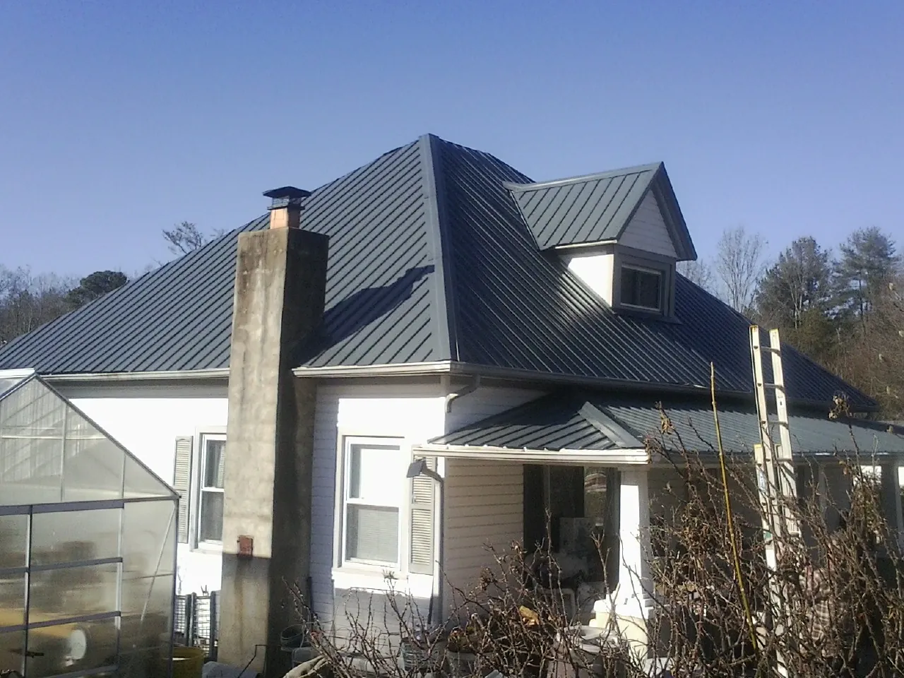 Dark blue standing seam metal roof on a white farmhouse with dormer — Slate & Tile Roof Repair by Roofing Brothers in Beaumont