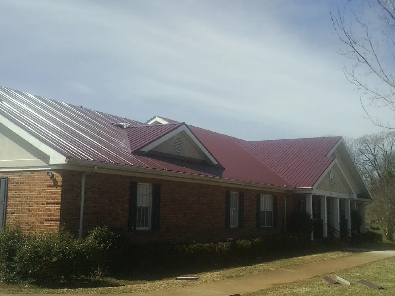 Red metal roof with gabled entries on a long brick building, from a Hail Damage Roof Repair job in Beaumont