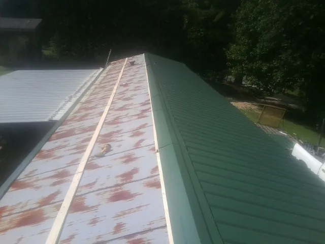 Old rusted panels beside newly installed green metal roofing — Wind Damage Roof Repair by Roofing Brothers in Beaumont